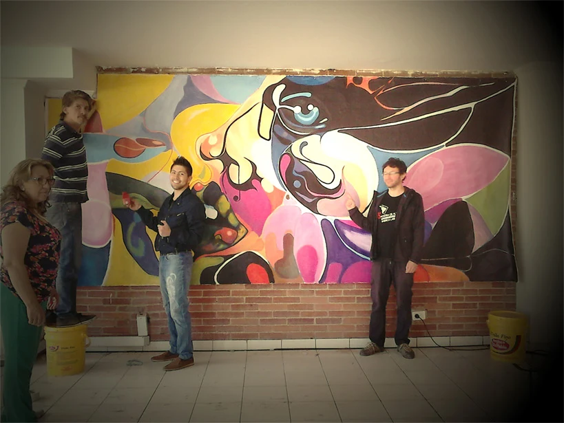Artists standing beside a large colorful abstract mural above a brick wall